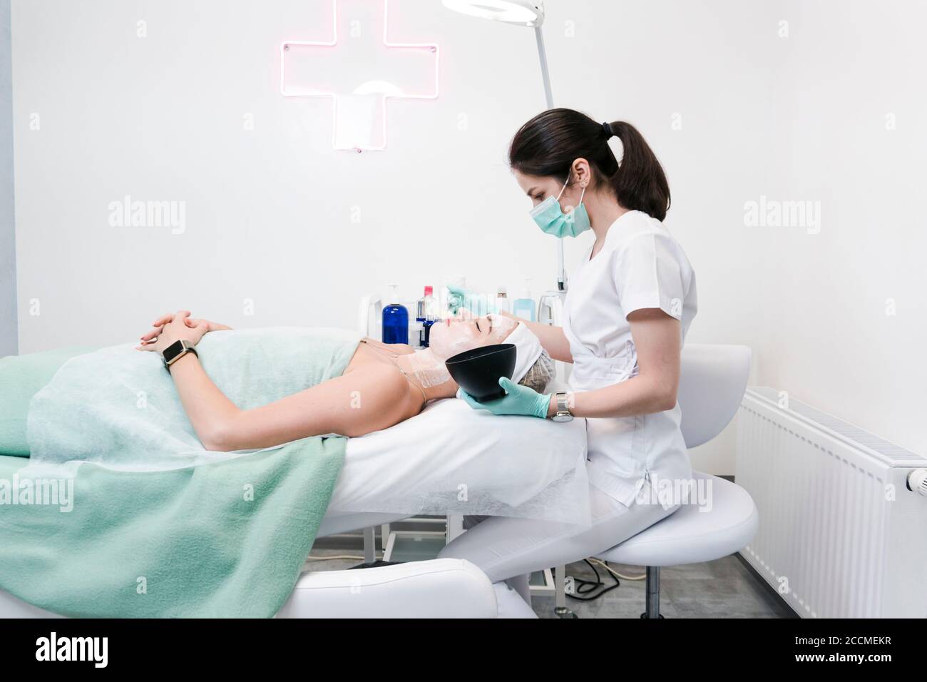 The young female client of cosmetic salon having a cleansing facial mask. The procedure of applying a peeling mask to the face. Concepts of skin care Stock Photo