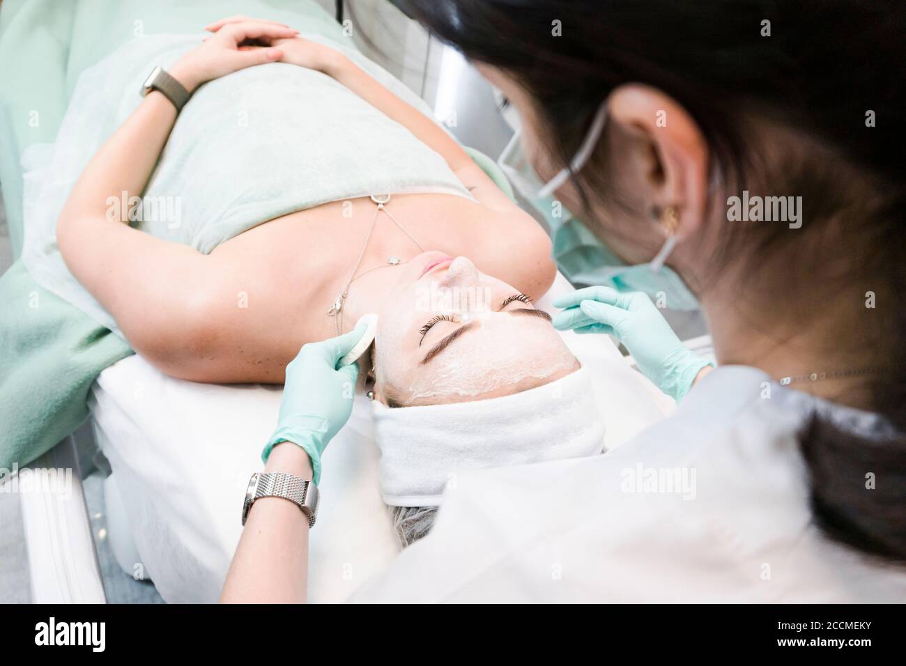 The young female client of cosmetic salon having a cleansing facial mask. The procedure of applying a peeling mask to the face. Concepts of skin care Stock Photo