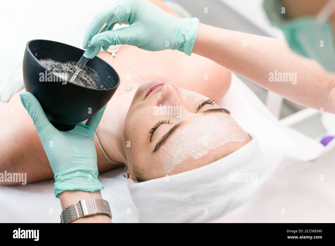 The young female client of cosmetic salon having a cleansing facial mask. The procedure of applying a peeling mask to the face. Concepts of skin care Stock Photo