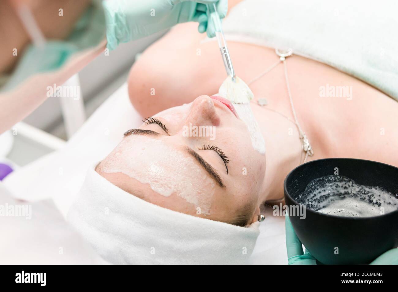The young female client of cosmetic salon having a cleansing facial mask. The procedure of applying a peeling mask to the face. Concepts of skin care Stock Photo