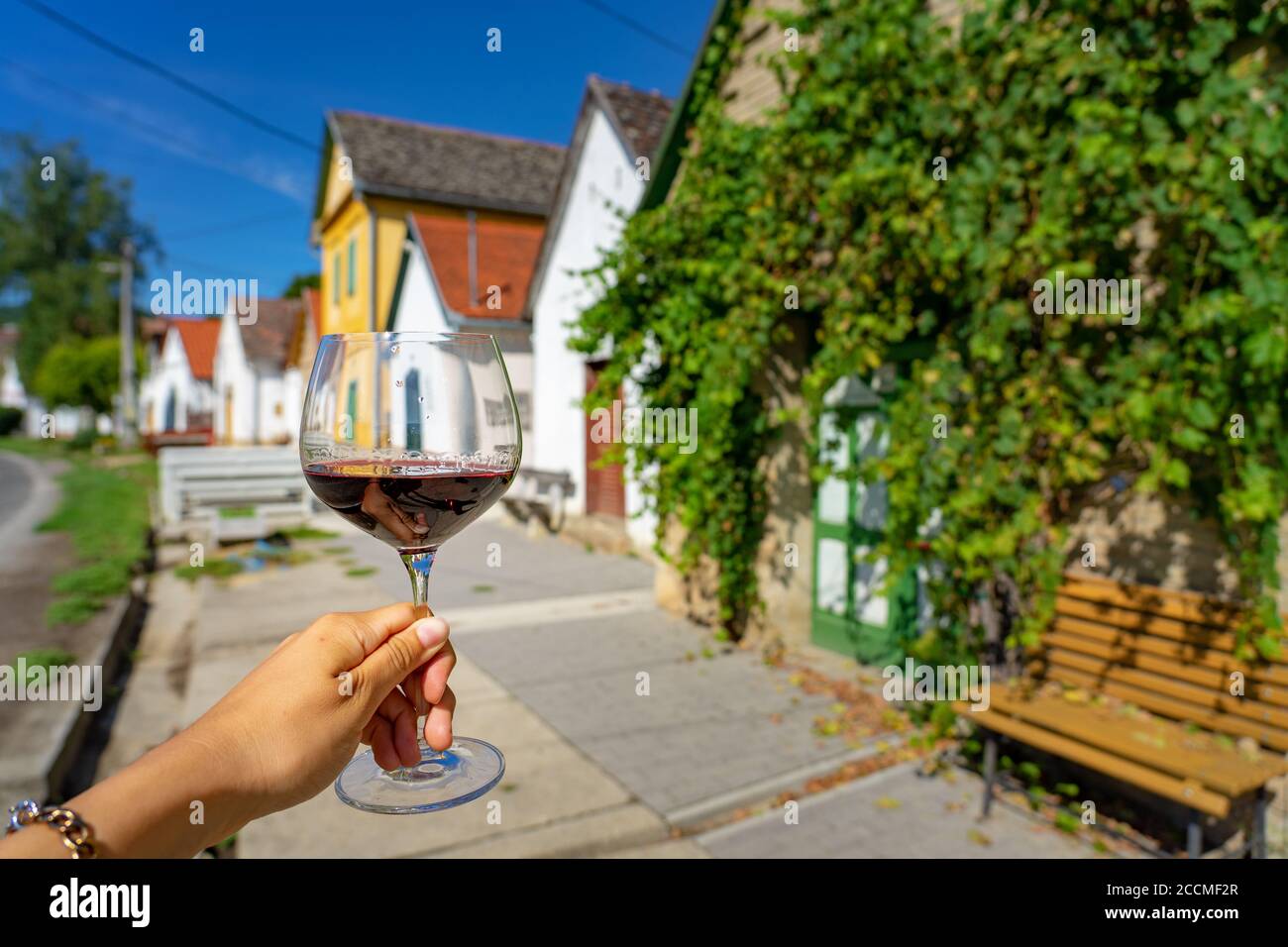 Glass of red wine with many colorful old traditional wine cellers in Villanykovesd in a hungarian wine region called Villany Stock Photo