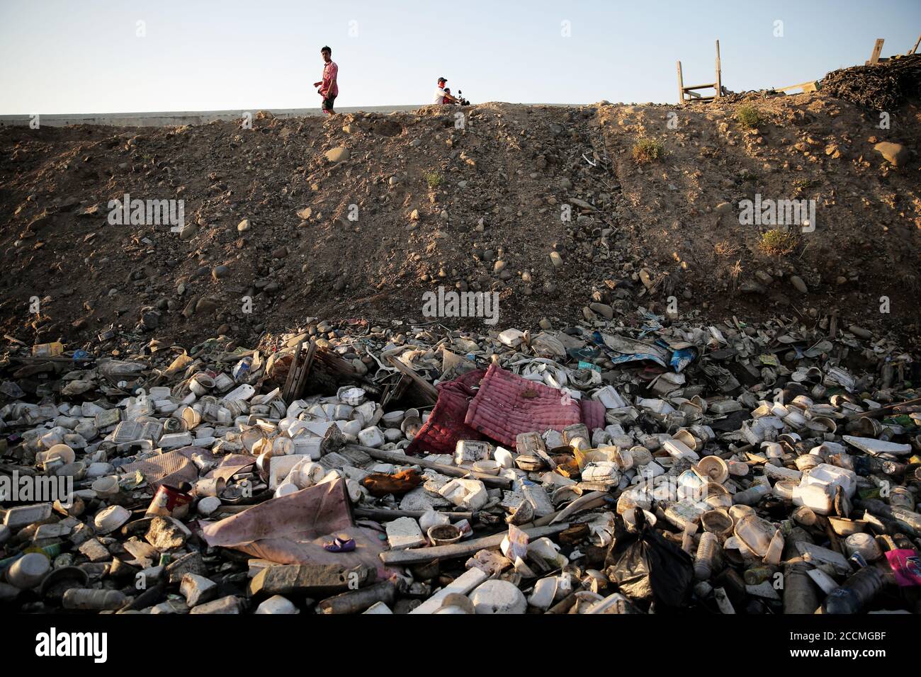 Residents walk past a pile of garbage.Plastic waste that has accumulated around the coast endangers marine life and local residents. Stock Photo
