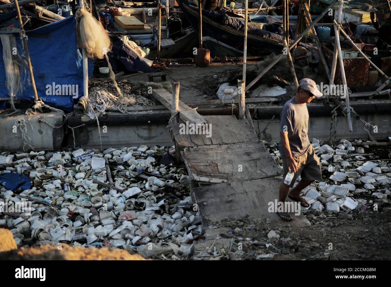 A man walks trough a pile of garbage.Plastic waste that has accumulated around the coast endangers marine life and local residents. Stock Photo