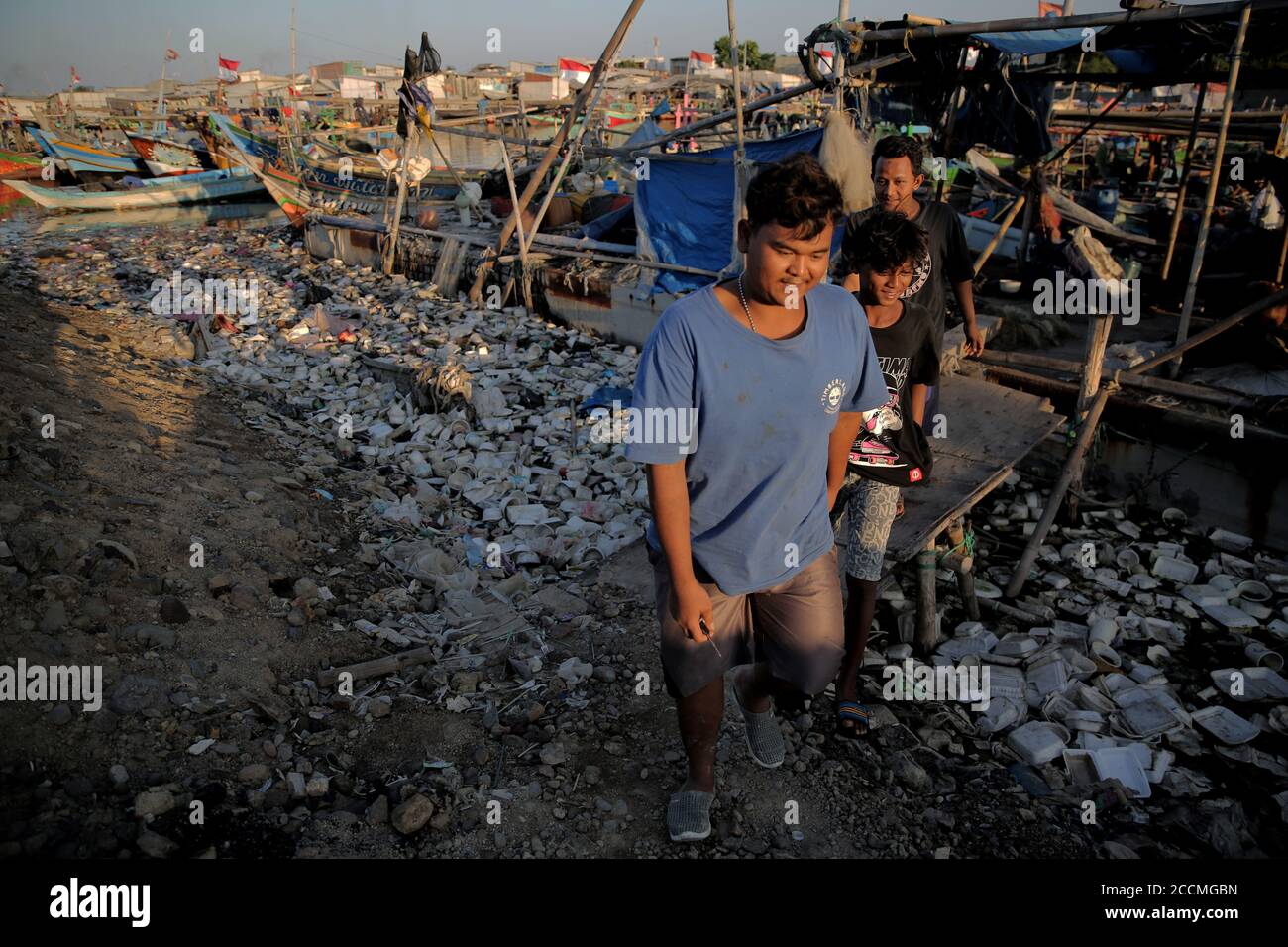 Residents walk through a pile of garbage.Plastic waste that has accumulated around the coast endangers marine life and local residents. Stock Photo