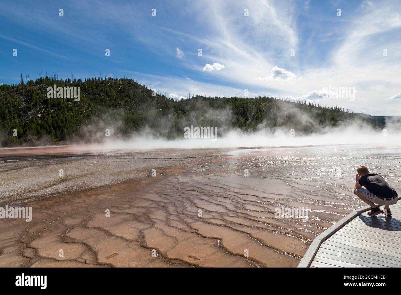 Yellowstone National Park, Wyoming / USA - July 22, 2014:  A young man squatting down to take a picture at Grand Prismatic Spring in Yellowstone Natio Stock Photo