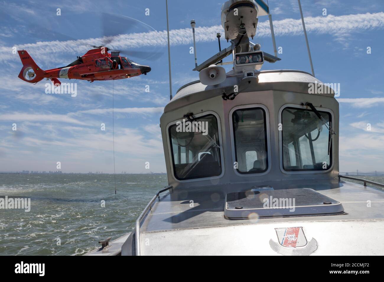 A trail line is lowered from a USCG MH-65 Dolphin helicopter as it approaches the USCG Auxiliary patrol vessel Silver Charm on San Francisco Bay Stock Photo