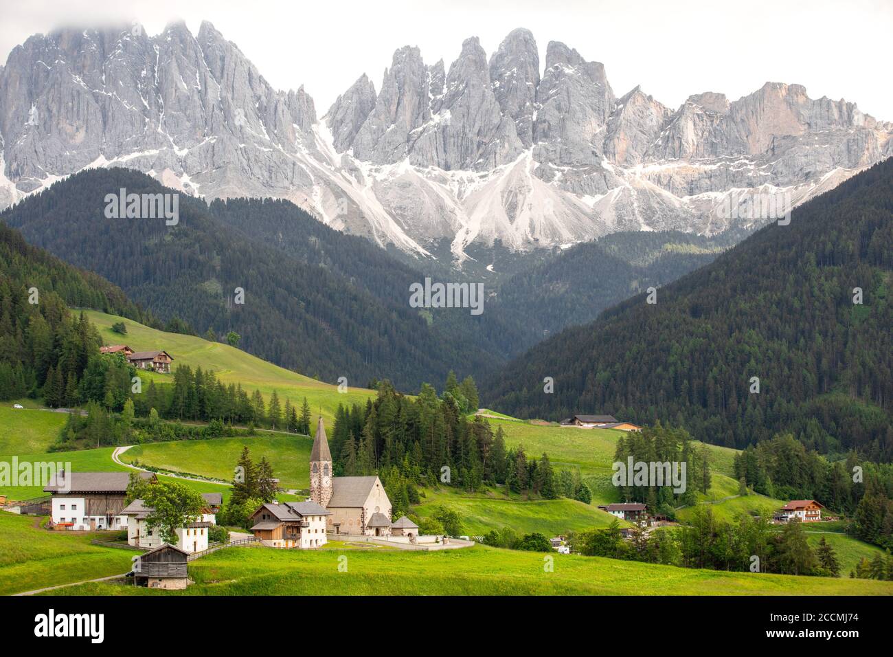 Iconic view of a northern Italian valley, with a small church surrounded by meadows and trees in the foreground and a mountain range in the background Stock Photo