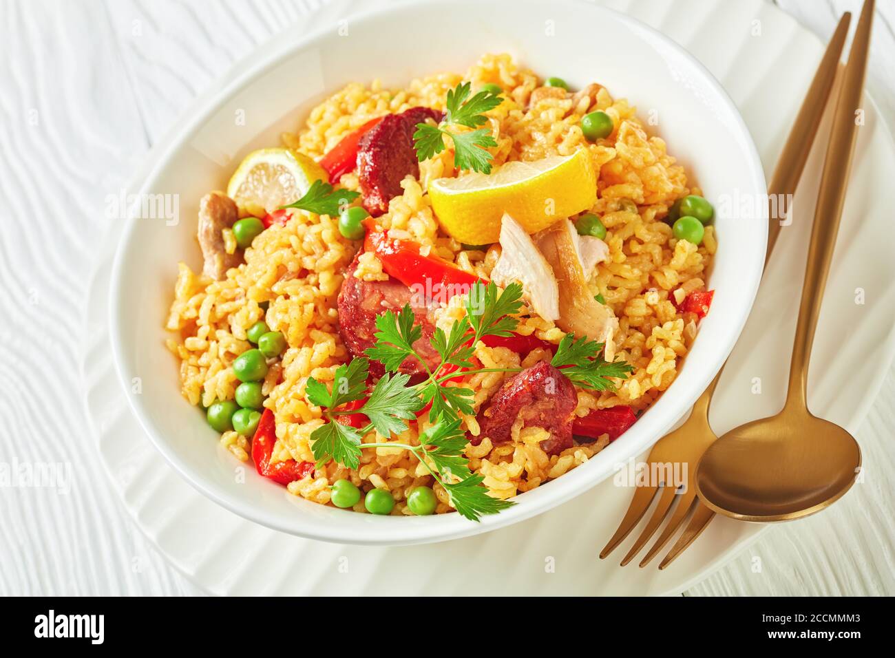 portion of spanish chicken paella with valencian bomba rice, chicken thigh meat, chorizo sausages, vegetables and spices served on a white plate on a Stock Photo