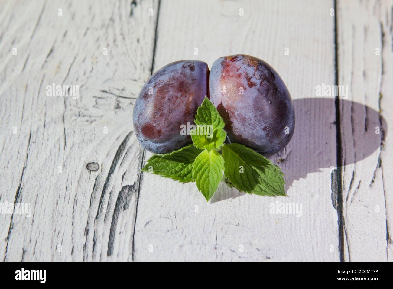 Trendy ugly organic fruit purple plum on the wooden background. Funny, deformed, unnormal fruit or food waste concept. Horizontal orientation.  Stock Photo