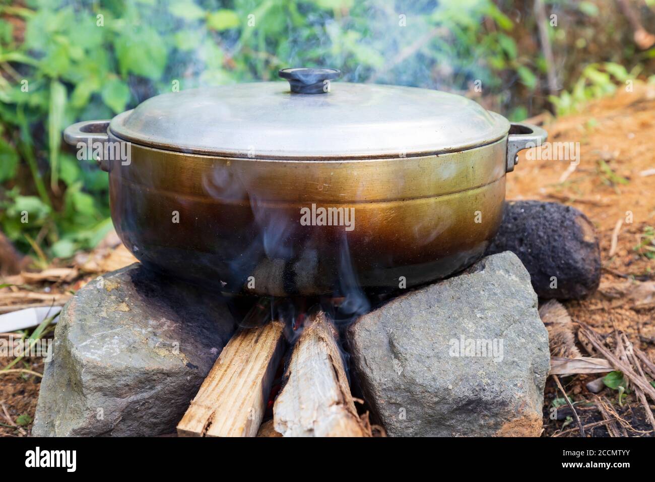 An aluminium pot on a wood fire restin gon two stones on the ground Stock Photo Alamy