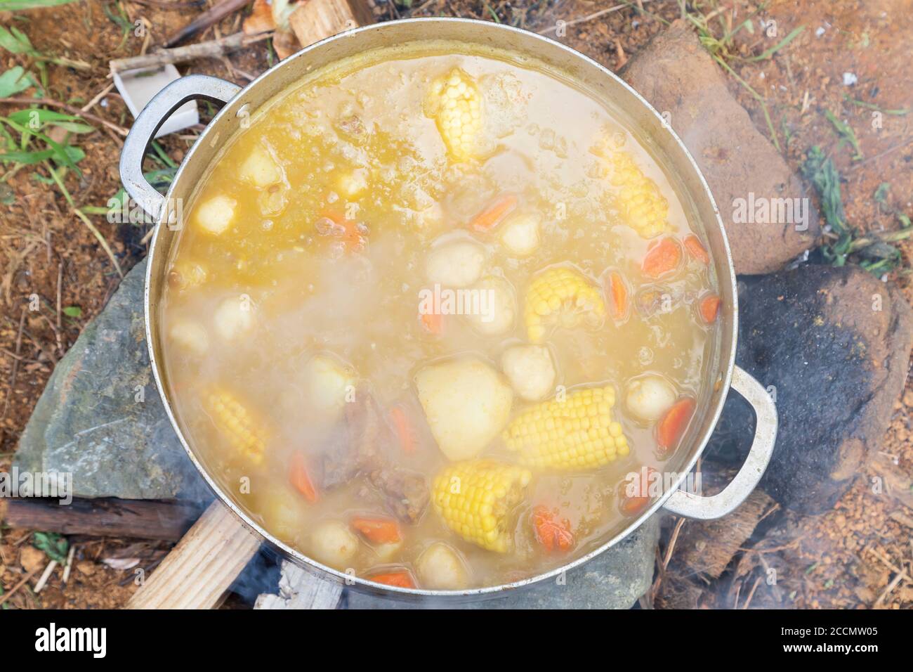 Corn, chicken, pumpkin, lentils and dumplins in a bouillion in an aluminium pot on a wood fire on the ground Stock Photo