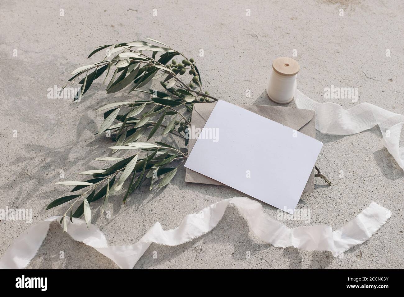 Summer wedding stationery mock-up scene. Blank greeting card, envelope, silk ribbon and olive branches and fruit in sunlight. Grunge concrete Stock Photo