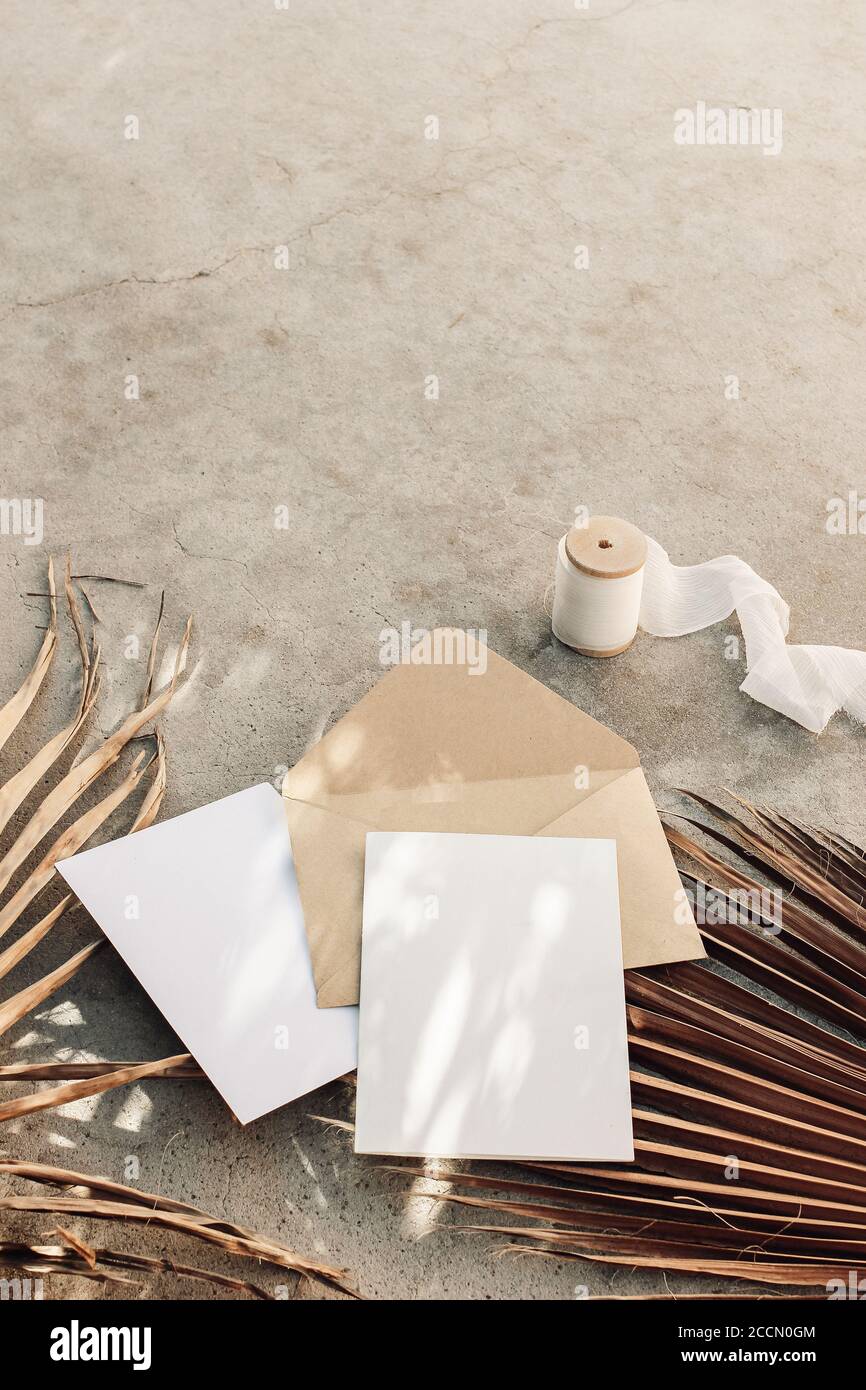 Summer boho wedding stationery still life. Blank greeting cards, envelope mock-ups and silk ribbon. Dry palm leaves on grunge concrete background Stock Photo