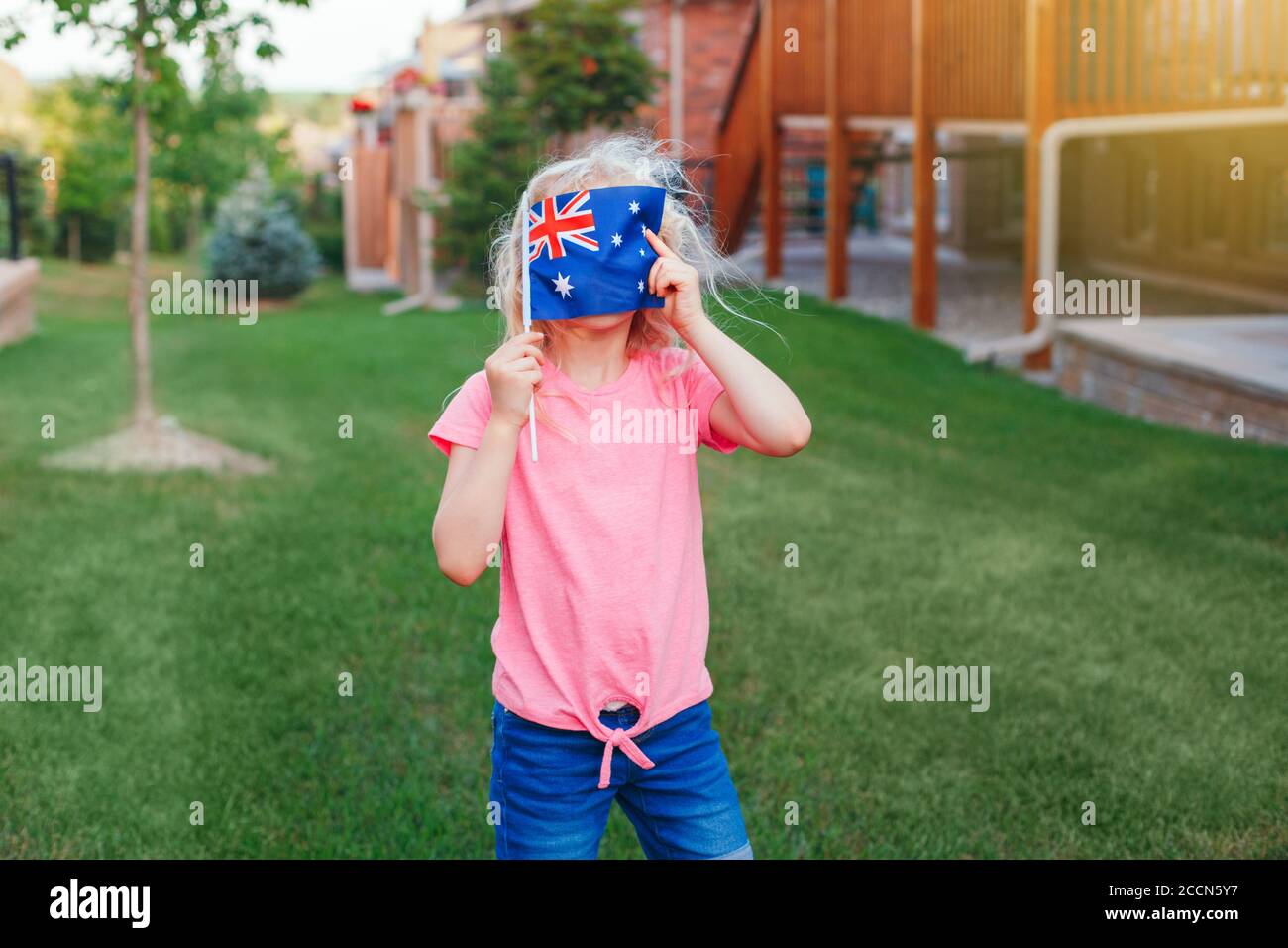 Adorable cute happy Caucasian girl holding Australian flag. Funny child kid covering her face with Australia flag. Little citizen celebrating Australi Stock Photo