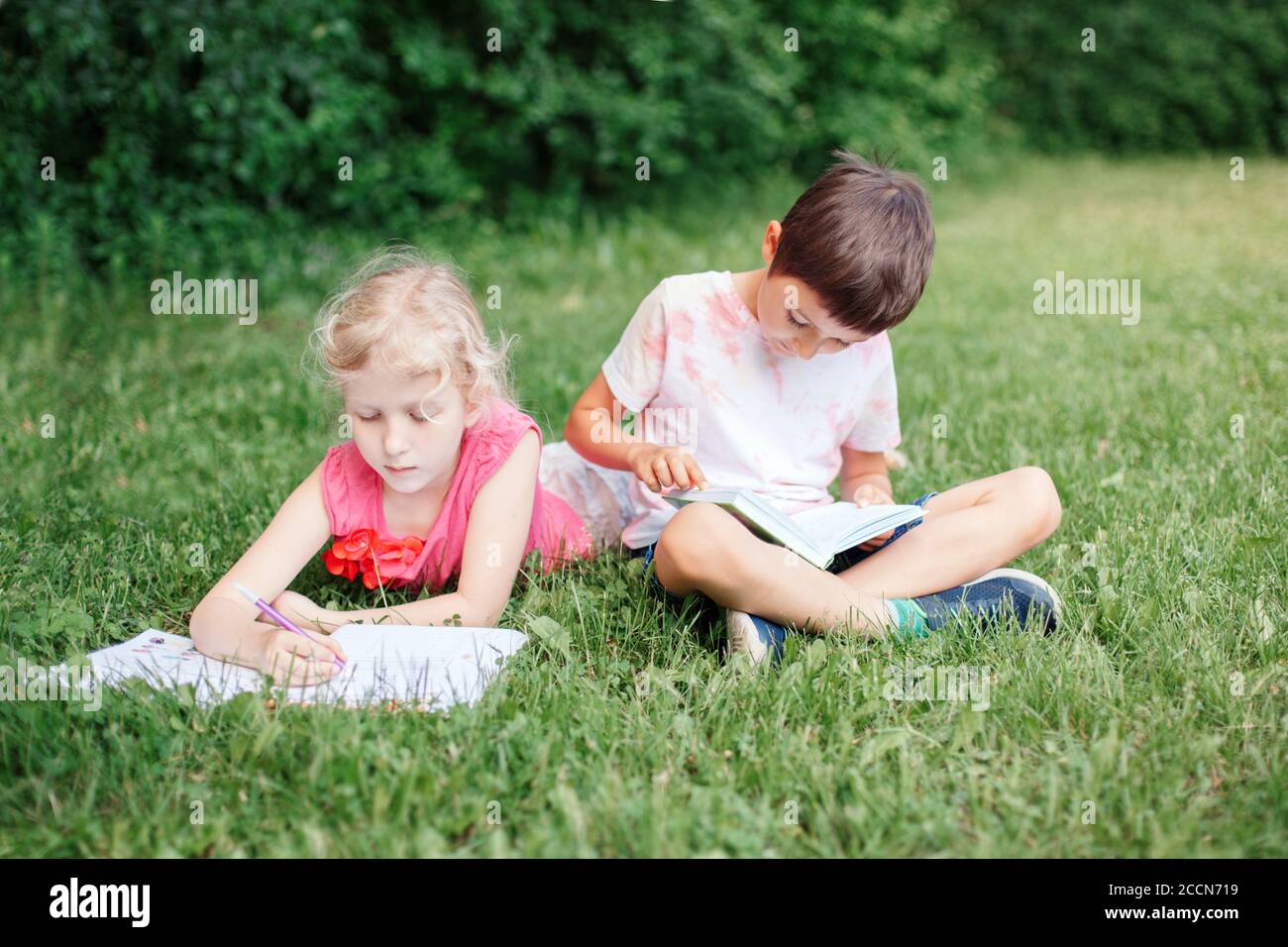 Elementary school students girl and boy doing homework outdoor. Children kids reading book and writing with pencil. Children education learning study Stock Photo