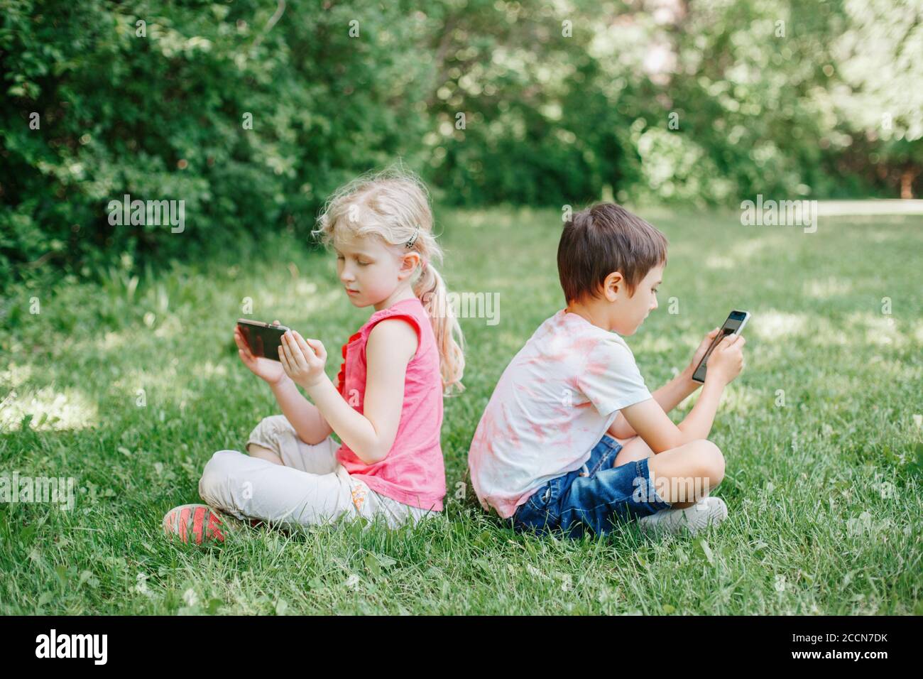 Boy and girl play games on smartphones outdoor. Kids digital gadget screen addiction. Children friends sitting on grass in park Stock Photo - Alamy