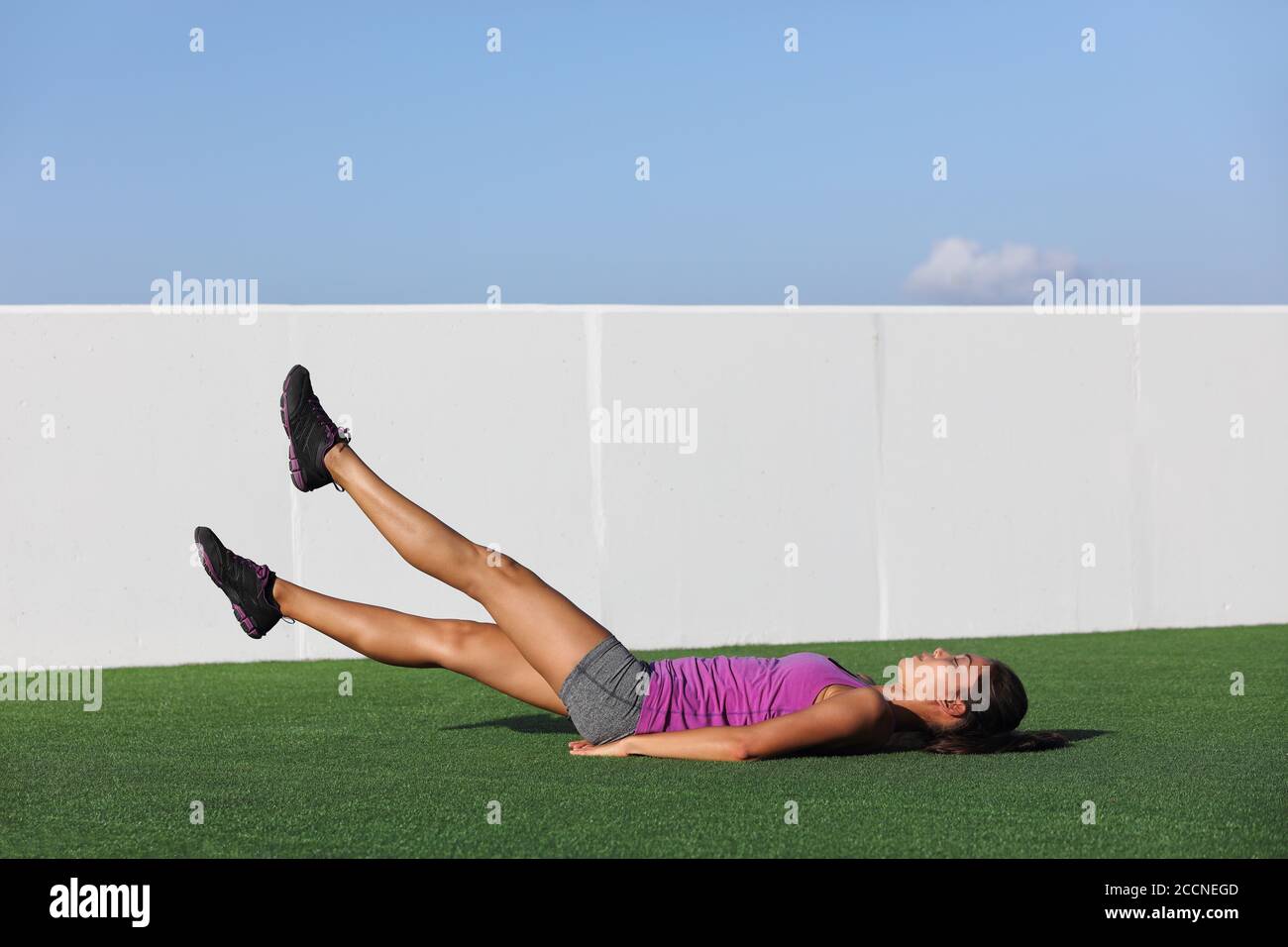 Fitness woman training abs workout doing scissor lifts leg raise or flutter kicks exercise out outdoor grass floor at gym Stock Photo