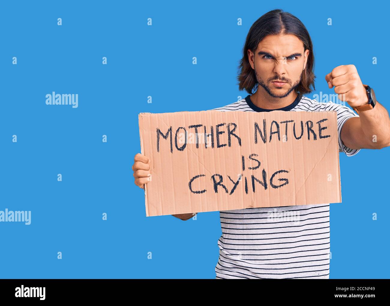 Young handsome man holding mother nature is crying protest cardboard banner annoyed and frustrated shouting with anger, yelling crazy with anger and h Stock Photo