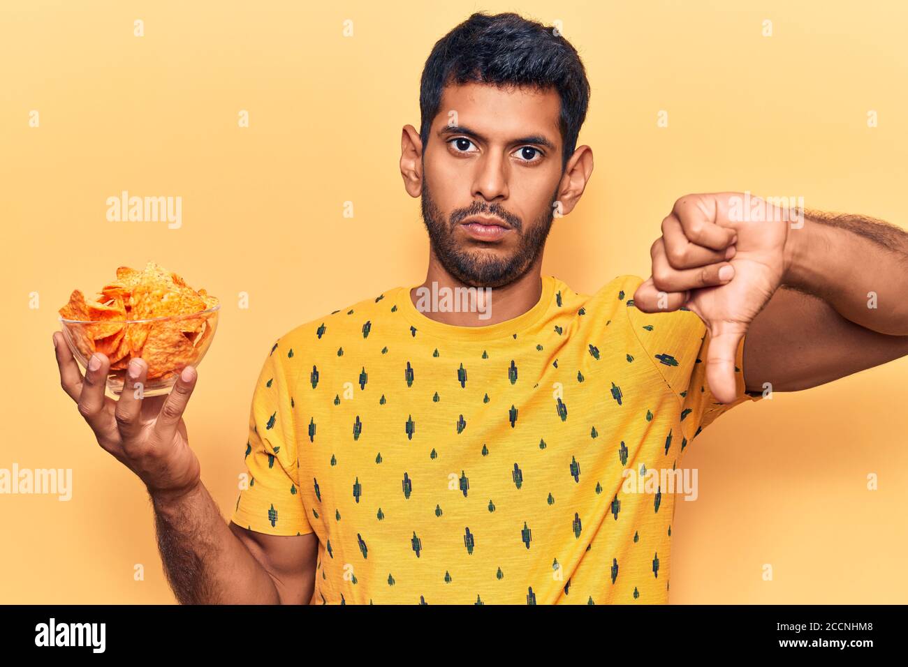 Young latin man holding nachos potato chips with angry face, negative ...