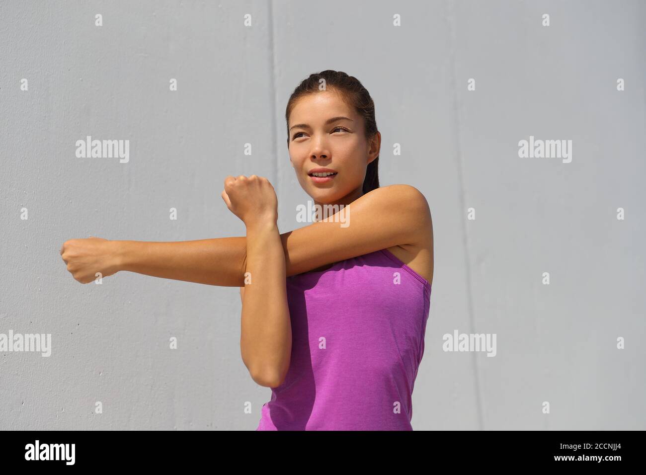 Fitness Asian runner doing warm-up stretching arms before jogging workout outdoor. Run race girl getting ready for running competition Stock Photo