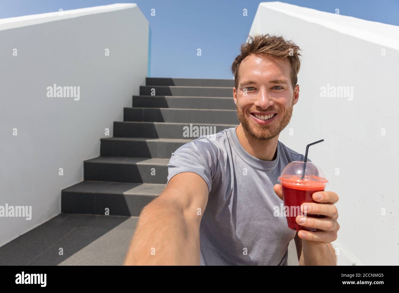 Healthy eating man drinking beet juice smoothie in urban city background. Active lifestyle fitness runner eating breakfast vegetable shake on stairs Stock Photo