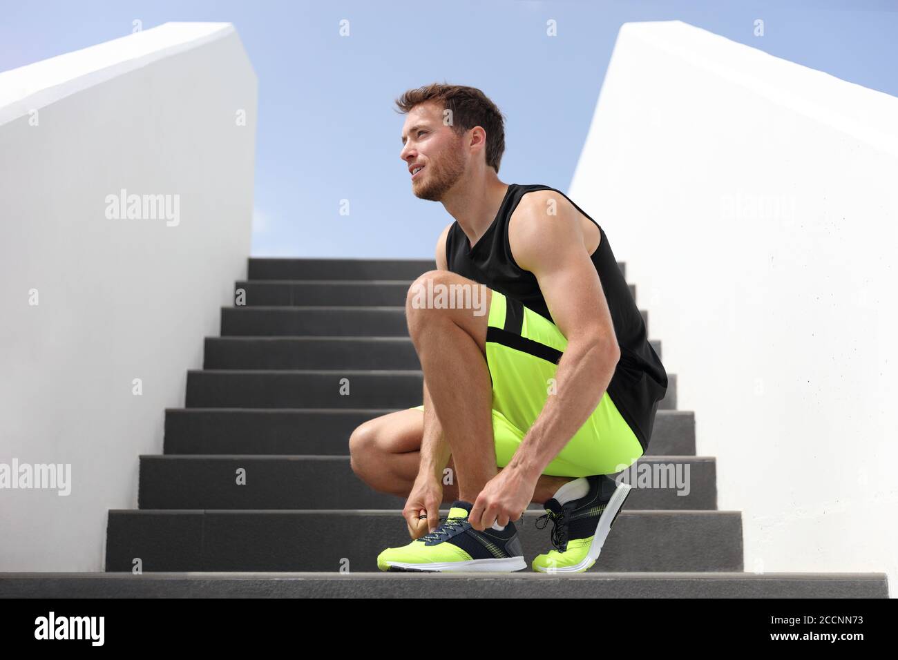 Runner man tying running shoes laces getting ready to run up the gym stairs training cardio hiit workout exercise on staircase. Acitve healthy Stock Photo