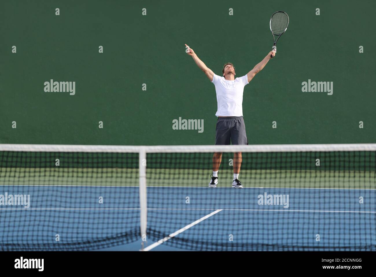 Tennis player man winning match happy excited with arms up in success on green outdoor court Stock Photo