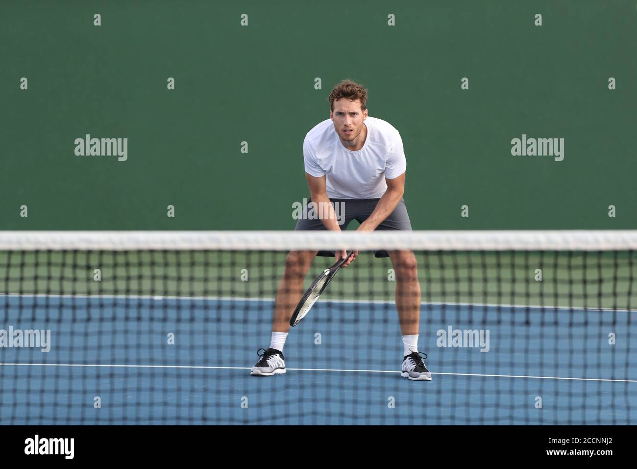 Professional tennis player man athlete waiting to receive ball, playing game on hard court. Fitness person focused behind net ready to return training Stock Photo