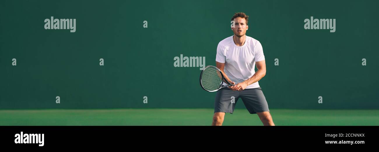 Tennis player man focused in ready position. A male athlete waiting for serve on panoramic green background banner. Challenge and concentration in Stock Photo