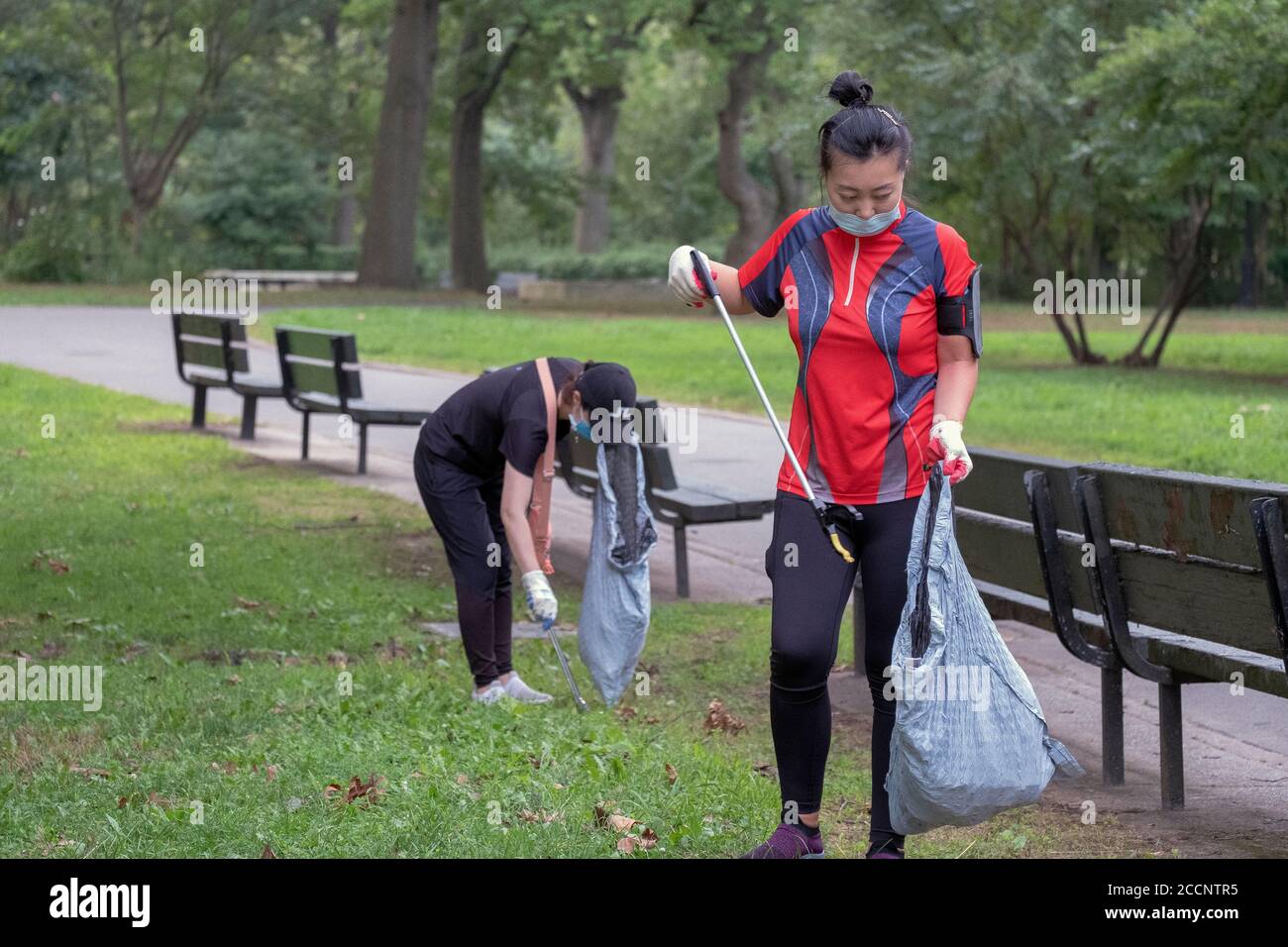 Two Asian American volunteers wearing face masks clean Kissena Park. In Flushing, Queens, New York City. Stock Photo