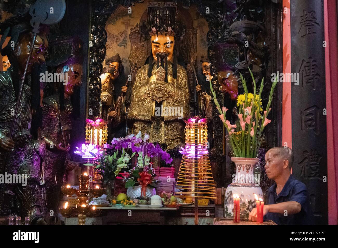 Altar inside a temple. Man arranging religious offerings and candles to a bearded sacred statue. Neon lights. Ngoc Hoang Pagoda, Ho Chi Minh, Vietnam Stock Photo