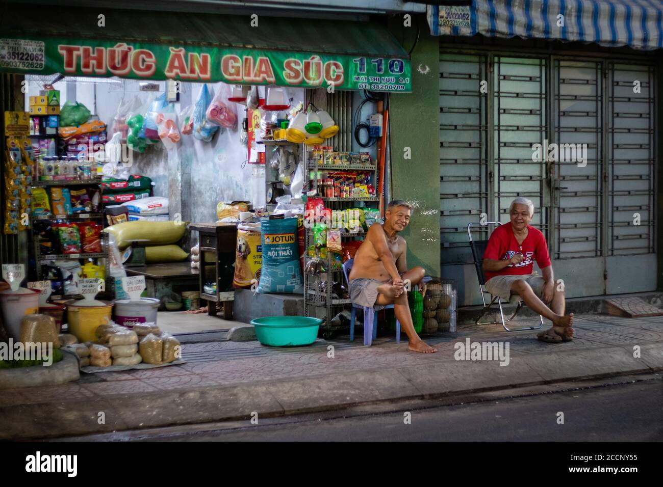 Processed pet food business open at night. Barefoot aged men chatting, chatting in front of the shop, sitting on chairs. Ho chi Minh, Saigon, Vietnam Stock Photo