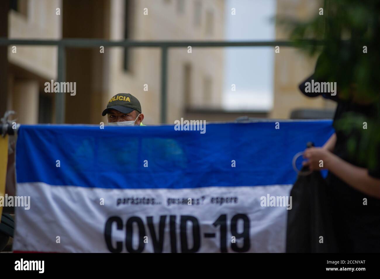 Bogota, Colombia. 23rd Aug, 2020. A police officer stands behing a sign with the message 'Parasites, worms, wait. COVID-19' during the Memorial Demonstrations for Dilan Cruz on August 23 2020 in Bogota, Colombia. Dilan Cruz was a high school student who was shot by a riot police officer during the 2019 national strike in Colombia, on the demonstrations that took place on november 23 2019. (Photo by Sebastian Barros Salamanca/Pacific Press) Credit: Pacific Press Media Production Corp./Alamy Live News Stock Photo