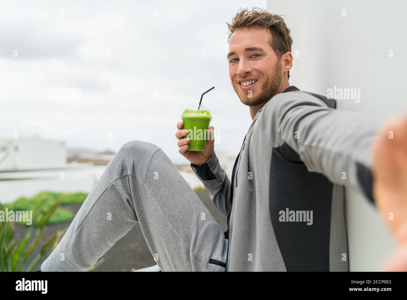Healthy green smoothie selfie sport fitness man taking self portrait picture at gym drinking vegetable juice after workout in sweatpants and Stock Photo