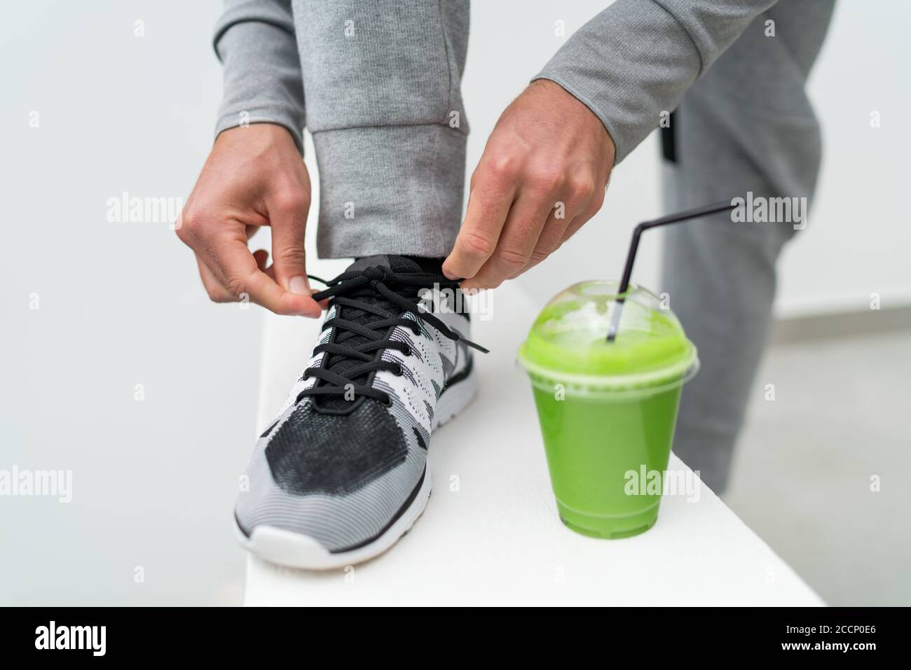 Fitness man tying running shoes and green smoothie breakfast. Health weight loss fitness man drinking green smoothie lacing trainers laces ready for Stock Photo