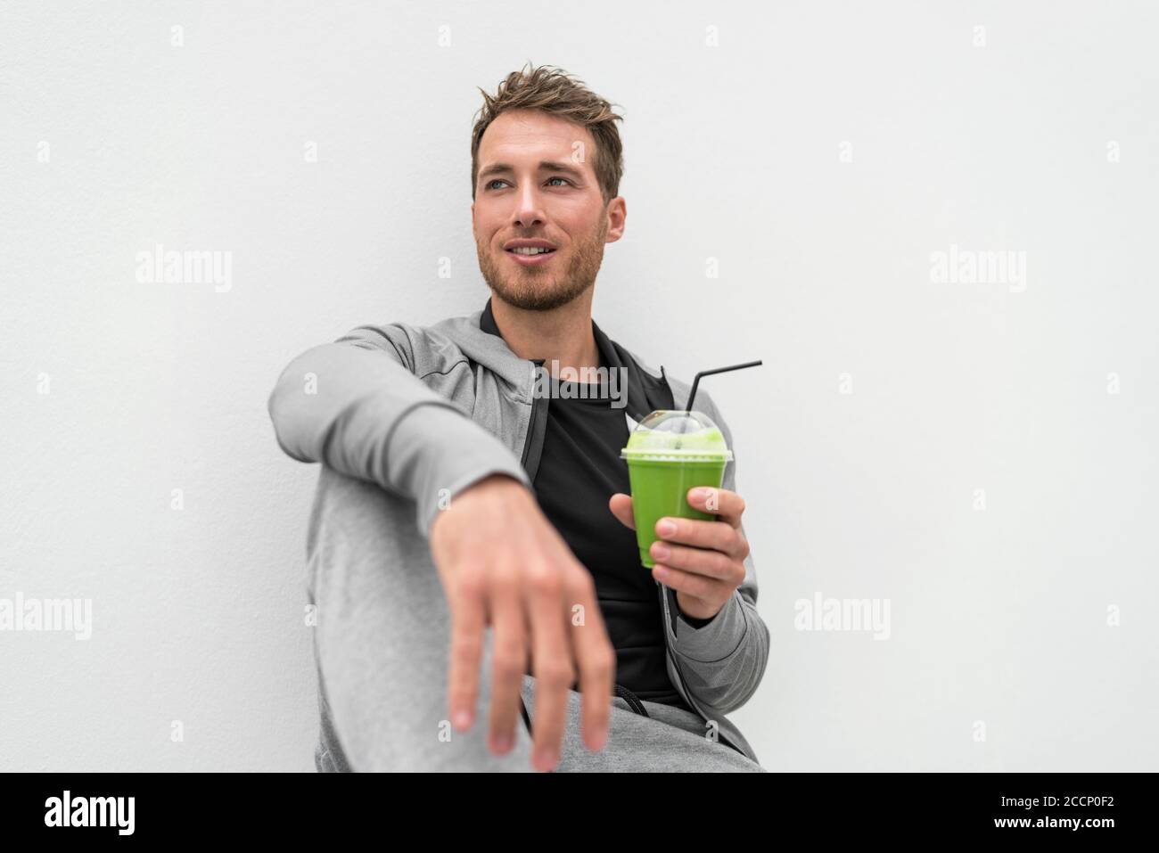 Healthy man drinking green smoothie spinach juice at home relaxing. Young adult eating detox diet, active lifestyle Stock Photo