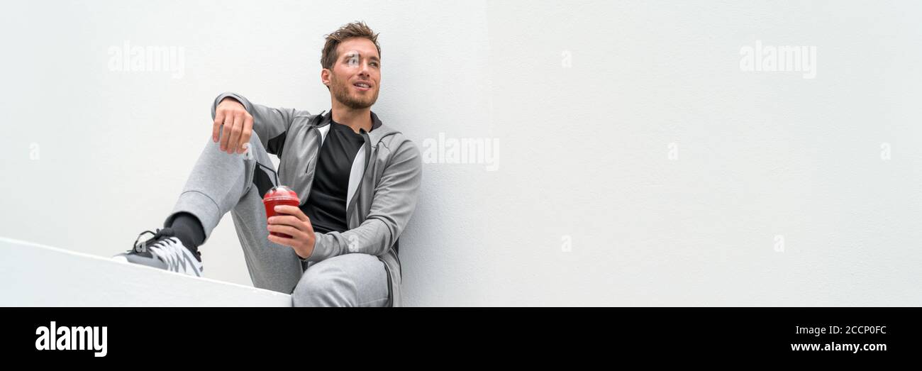 Healthy sport man drinking red smoothie breakfast juice banner panoramic crop relaxing sitting at home in casual activewear sitting on outdoor gym Stock Photo