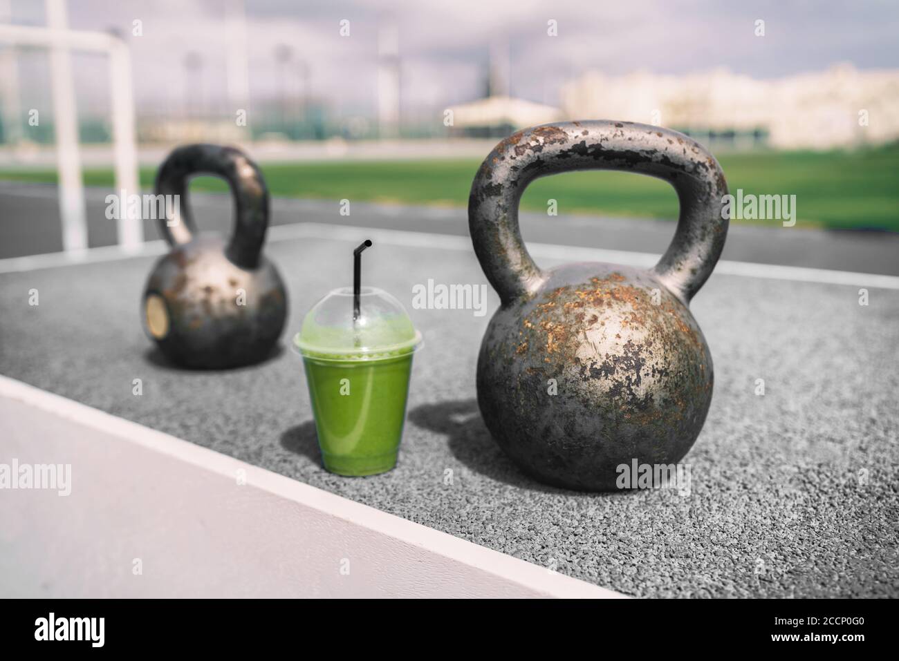 Health and fitness green smoothie detox drink at gym with kettlebells weights at outdoor training fitness center. Plastic cup of vegetable juice Stock Photo