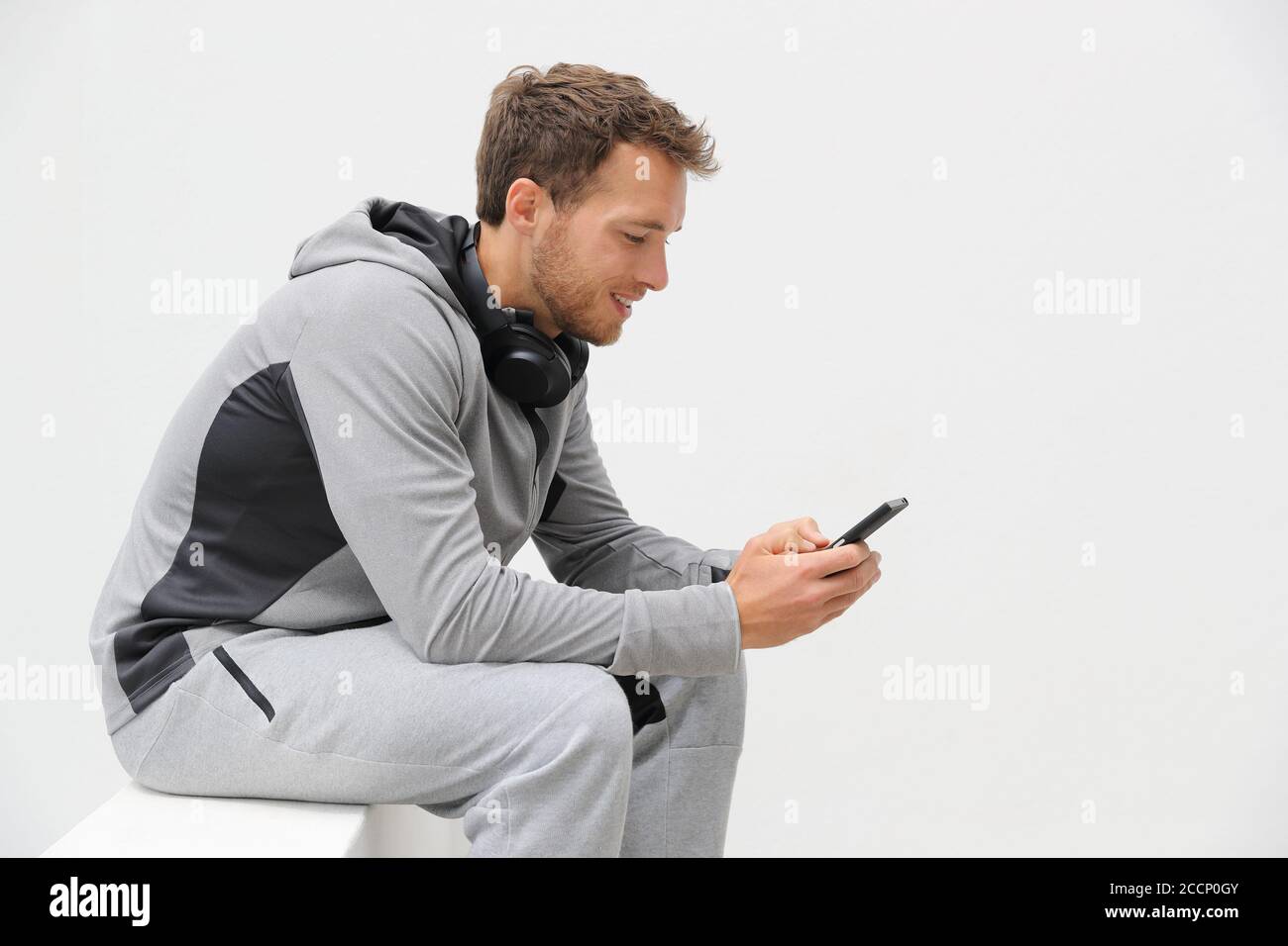 Fitness man using phone app on jogging break relaxing at home outdoors. Active lifestyle young adult holding smartphone watching online video or Stock Photo