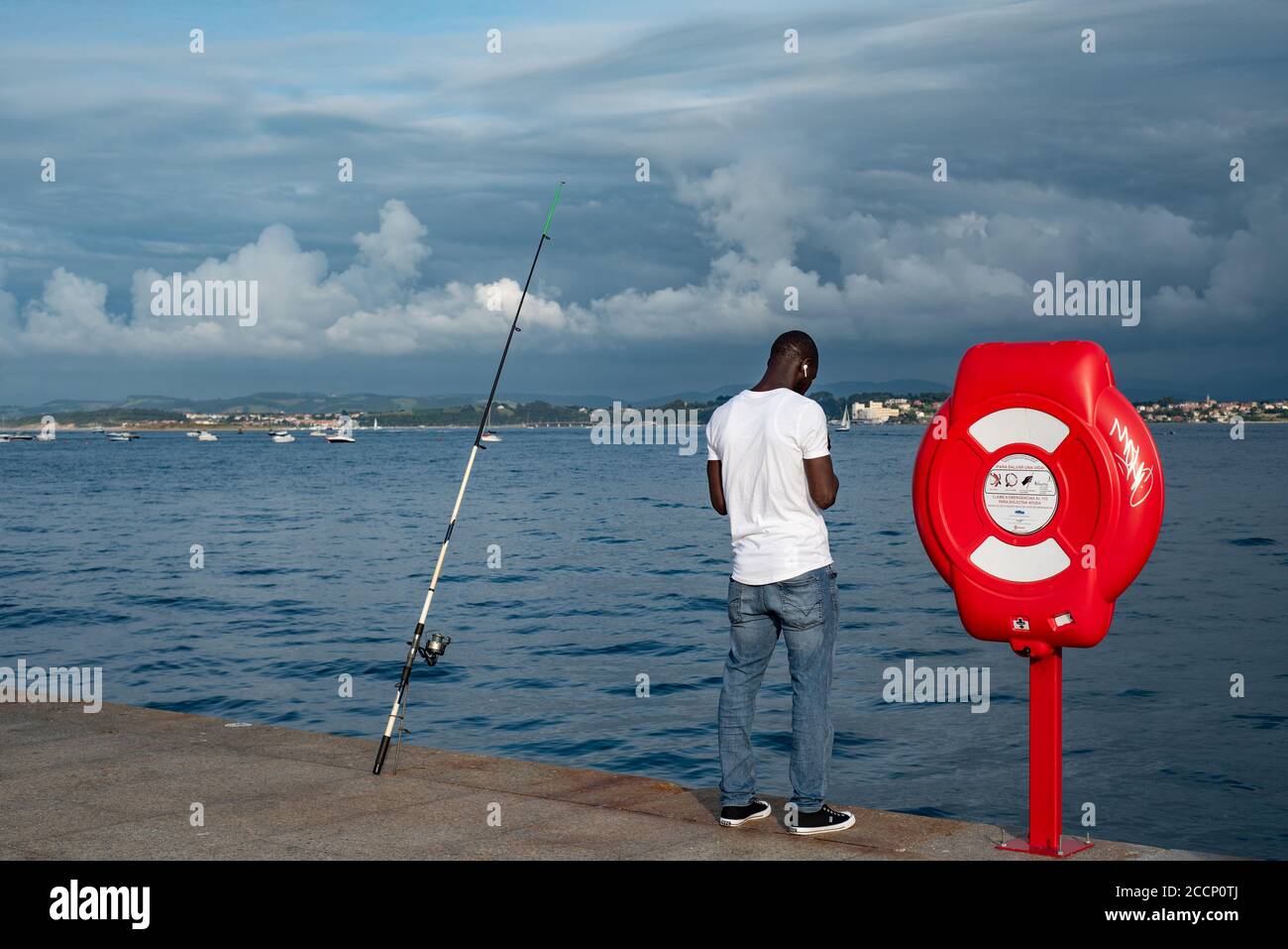 Rear view of a young black man wearing a white T shirt. Black man listening to music while fishing in Paseo Maritimo, Santander, Spain Stock Photo