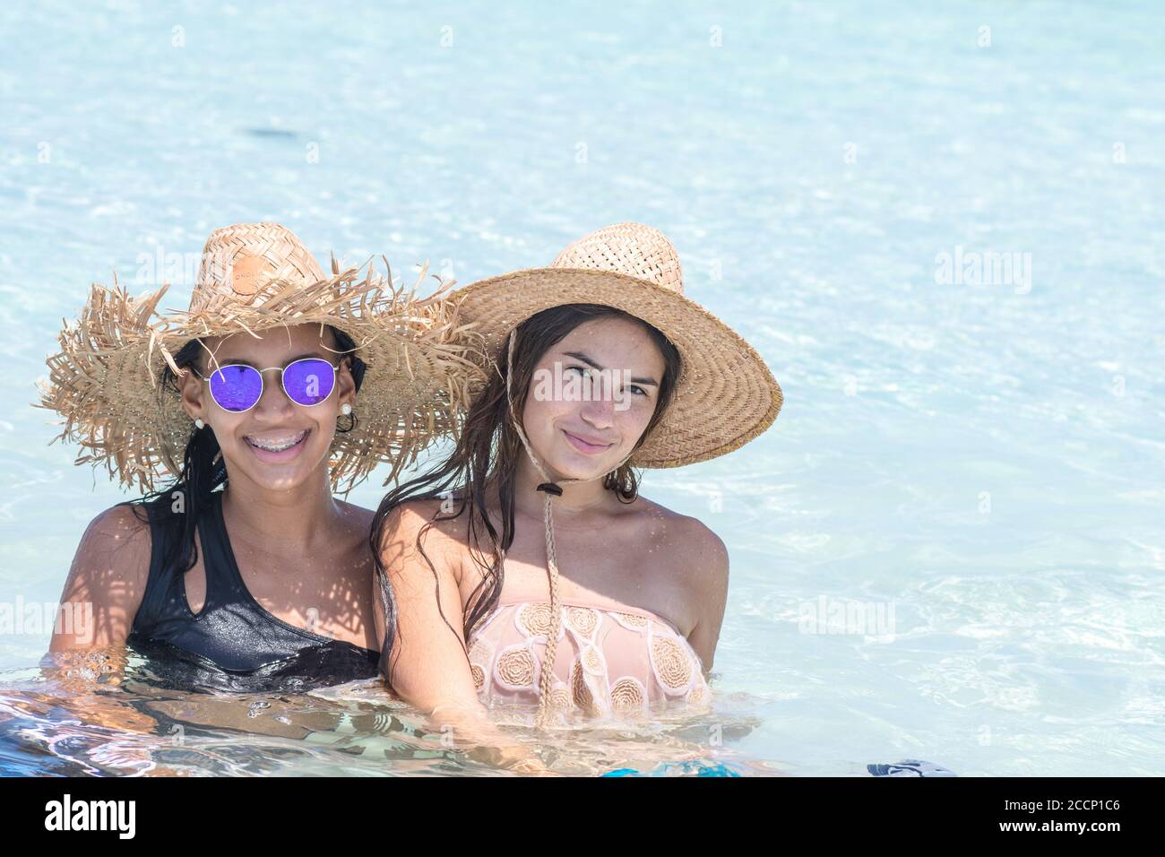 Girls latin american friends with hat enjoying sitting inside water in sunny day at Los Roques Venezuela Stock Photo