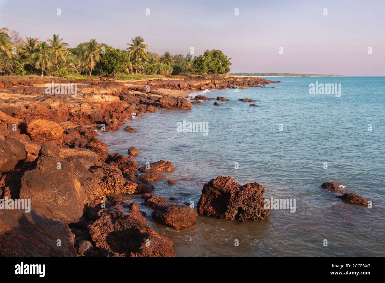 Unspoiled beach at sunset time. Rocky landscape, green trees and palm trees. Coastline of Timor sea. No people in the picture. Dundee Beach. Australia Stock Photo