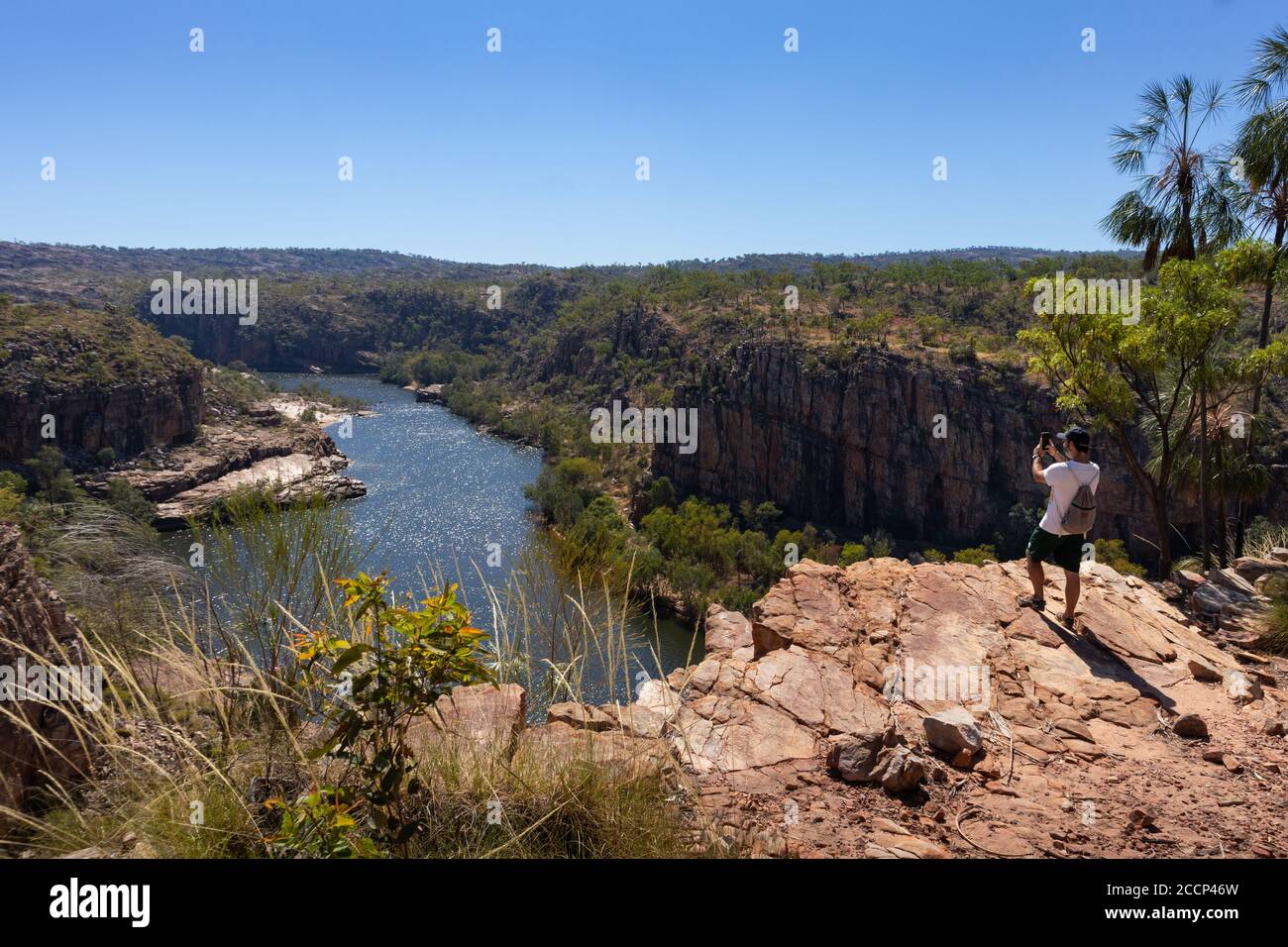 Man taking a picture of Katherine river with his smartphone. Rock platform above. Tourist with cap and neutral clothes. Katherine gorge, Australia Stock Photo