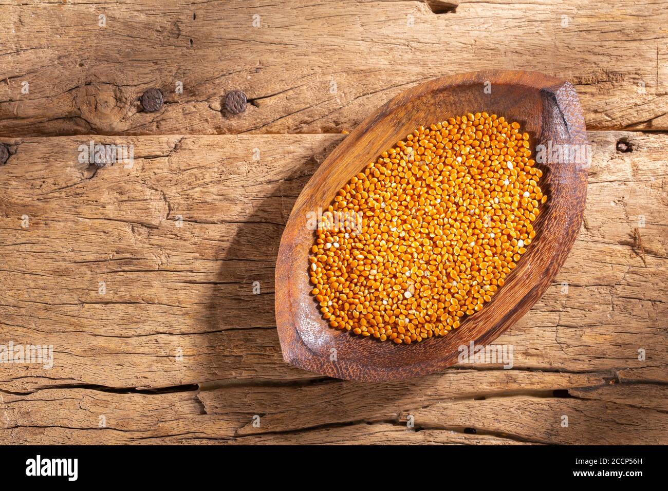 red millet grains in bowl on wood (Panicum miliaceum) Stock Photo