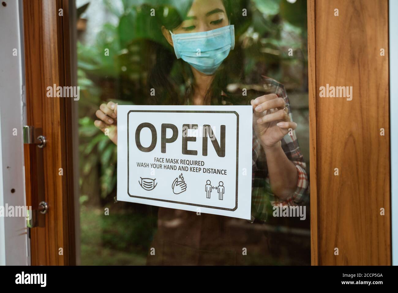 asian woman with open sign in her shop during covid-19 pandemic. new normal life keep your distance sign Stock Photo