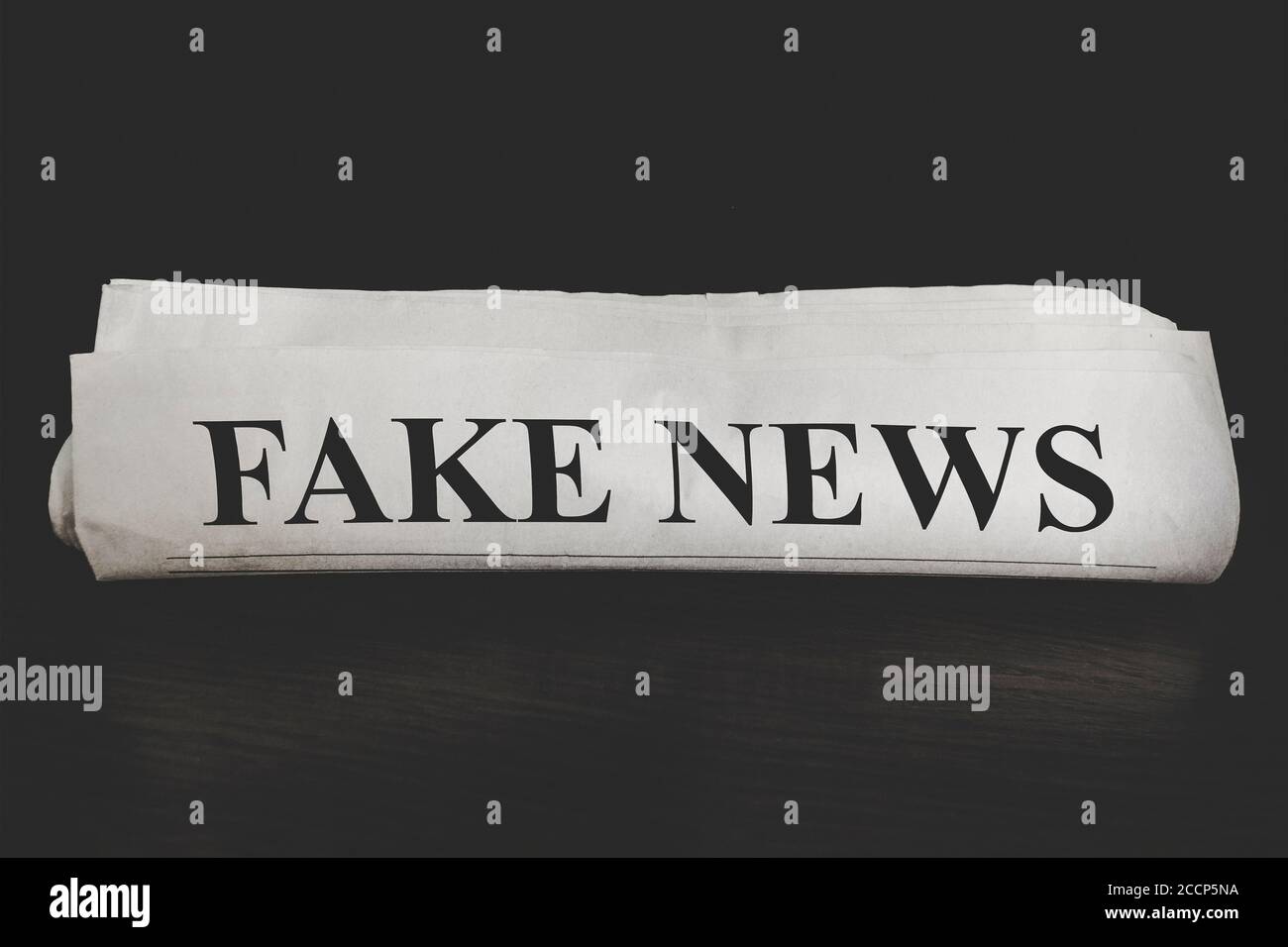 concept of false news. Fake News Newspaper on desk in office. Rolled Up Newspaper on dark background Stock Photo
