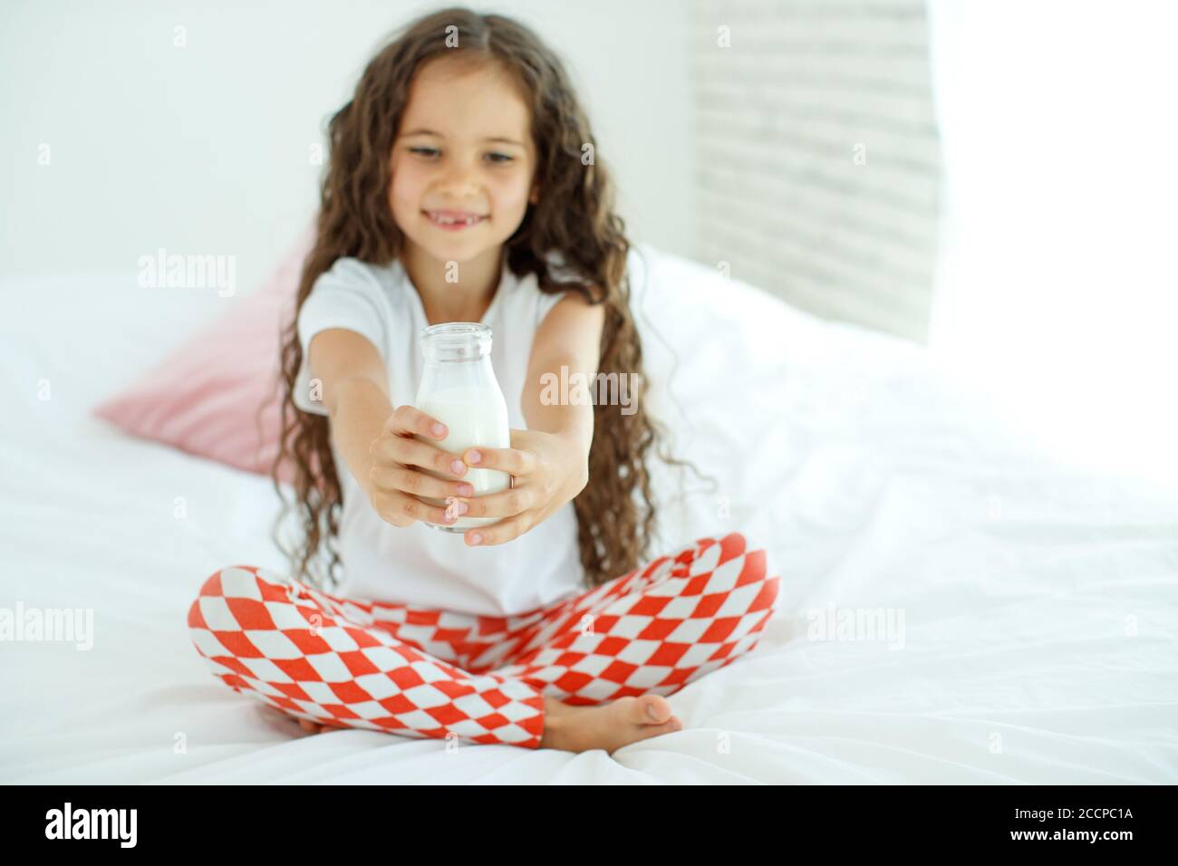 The baby is drinking milk. A little girl at home on the bed drinks