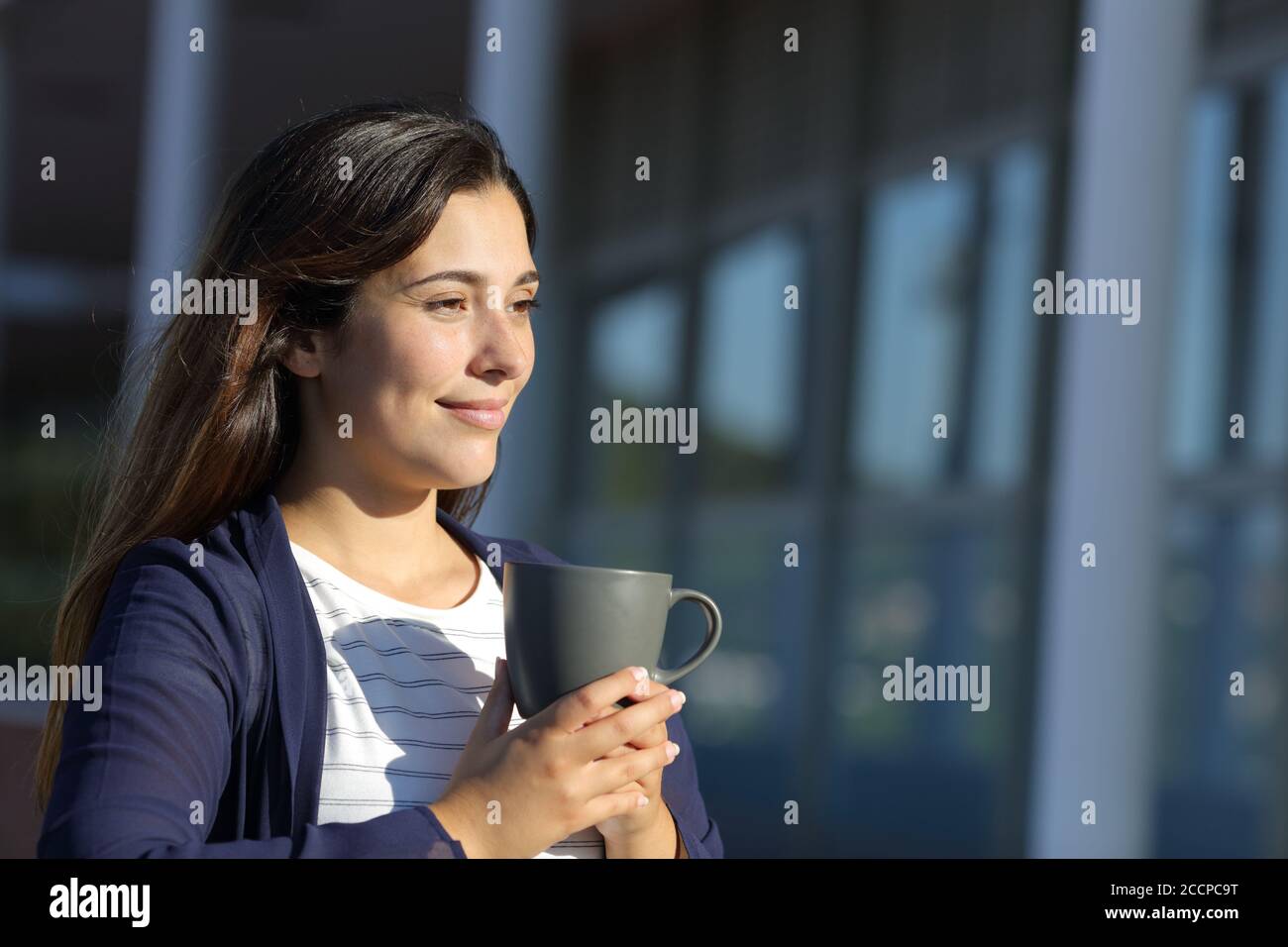 Woman drinks coffee in a terrace looking away a sunny day Stock Photo