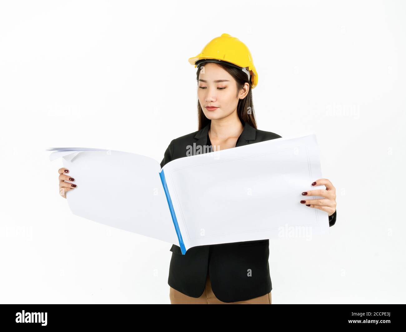 Young Asian businesswoman wearing black suit and yellow safety helmet checking project engineering paper plans in hands. Portrait of female engineer l Stock Photo