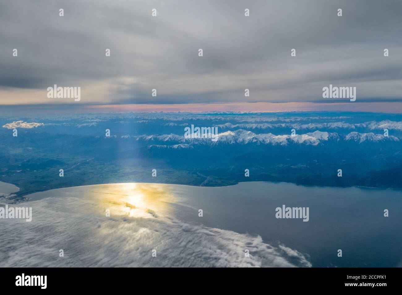 Flying over the open ocean with views of the east coast of New Zealand's South Island the clouds cover the sunset. Just a glimpse of the sun comes thr Stock Photo